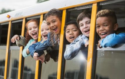 Little kids smiling out the window of school bus