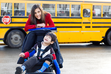 Special needs child in stroller in front of yellow school bus
