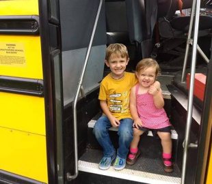 Two young kids sitting on the steps of yellow school bus