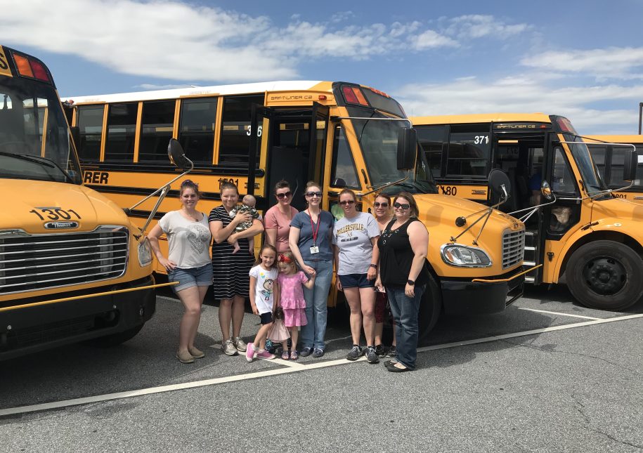 Family standing in front of parking school busses