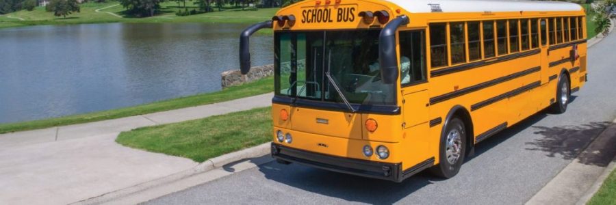 yellow school bus driving down the road near lake