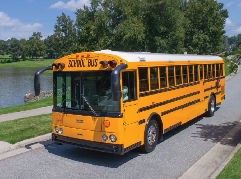 yellow school bus driving down road near lake